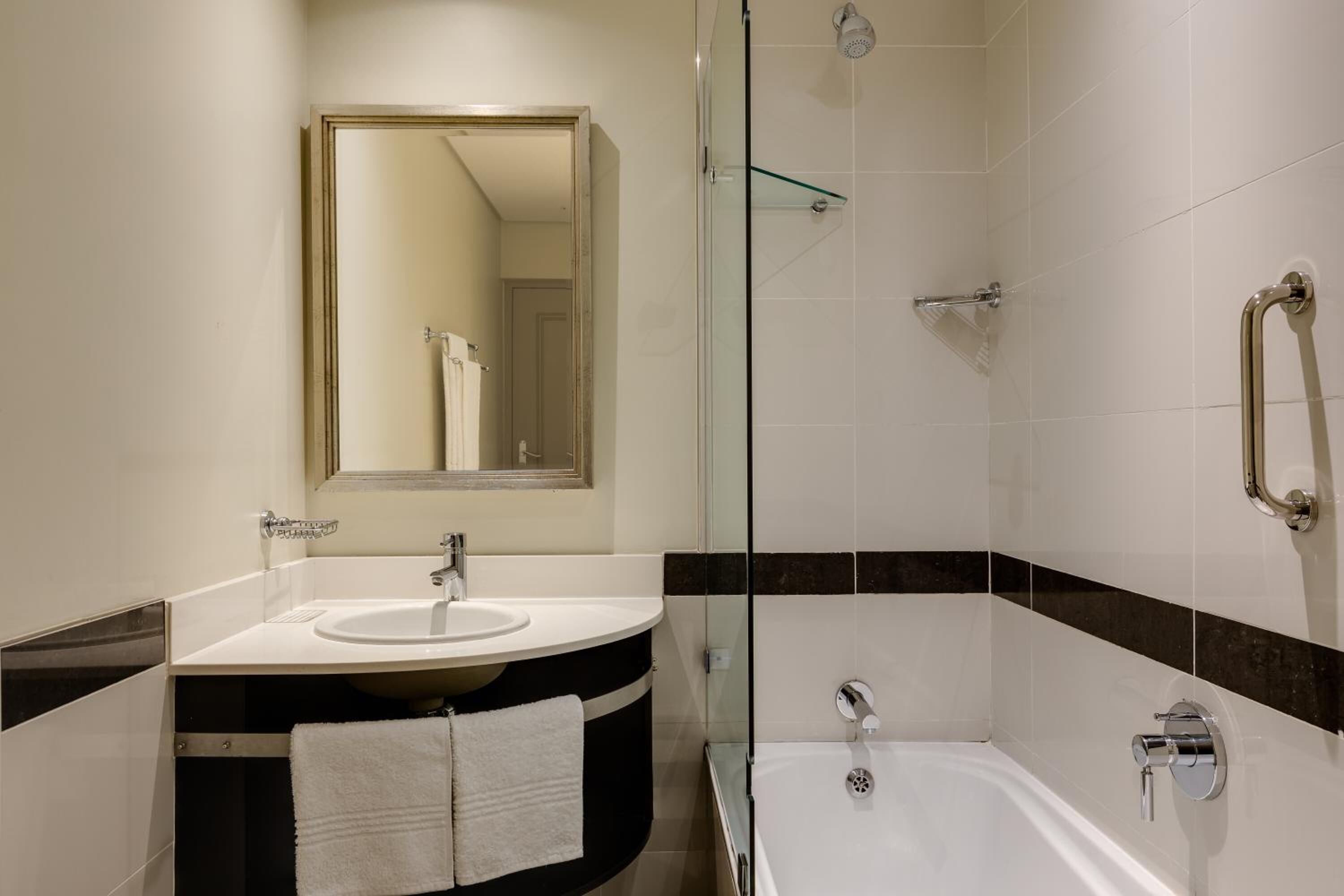 A modern bathroom with a glass-enclosed shower, a sink with a mirror above it, and a bathtub.