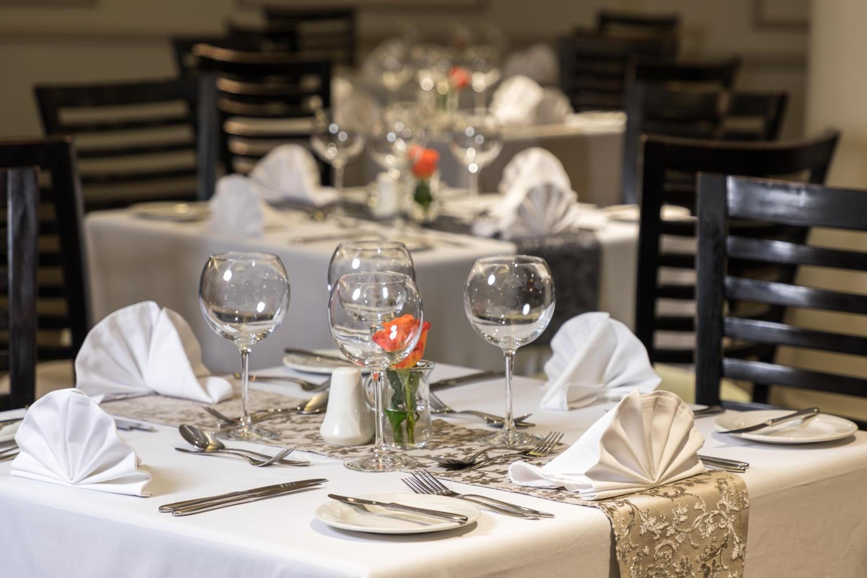 A dining table set for a formal meal with white tablecloths, silverware, and wine glasses.