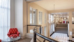 Un hall d’hôtel avec un fauteuil rouge, une table en verre et un escalier doté d’une rampe noire.