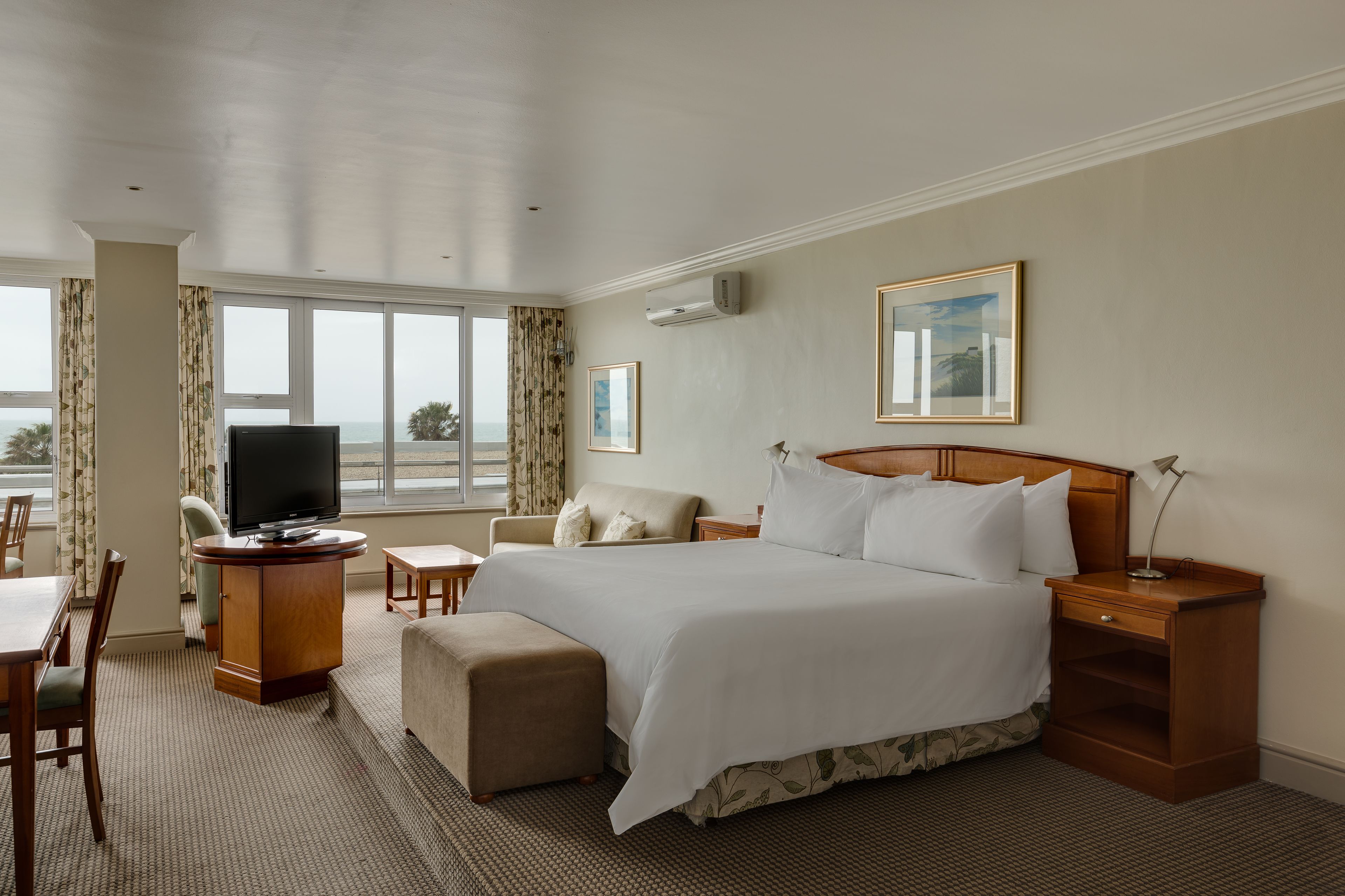 Habitación de hotel con una cama grande, un escritorio con televisor, una silla, una mesita y una ventana con cortinas.