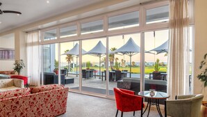 Une pièce spacieuse avec de grandes fenêtres, un canapé rouge à motifs et une table avec des chaises.