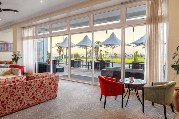 A spacious room with large windows, a red patterned sofa, and a table with chairs. - Southern Sun The Marine (Gqeberha (Port Elizabeth))