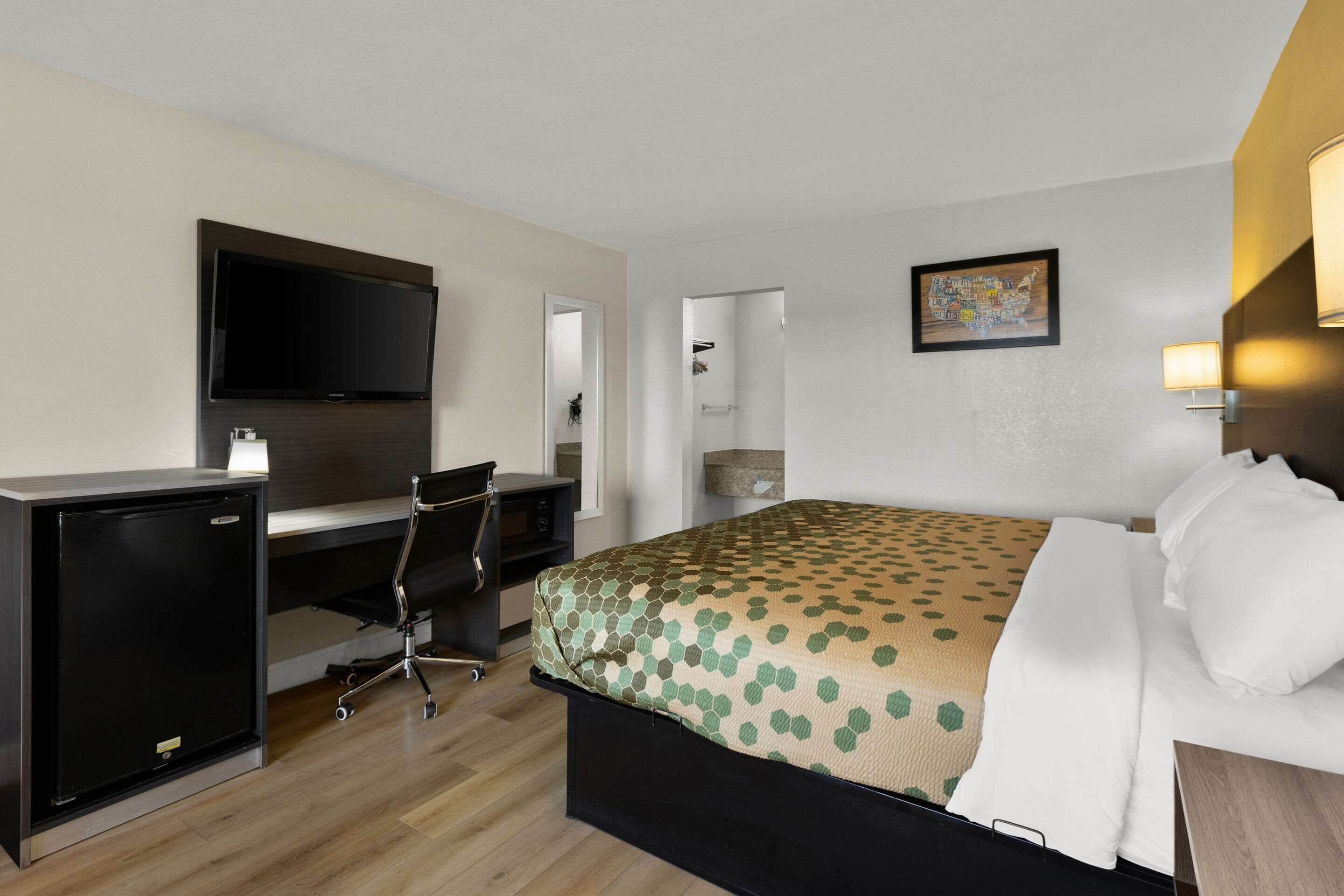 Ein Hotelzimmer mit einem Bett, einem Schreibtisch mit Computer, einem Fernseher und einer Dusche.