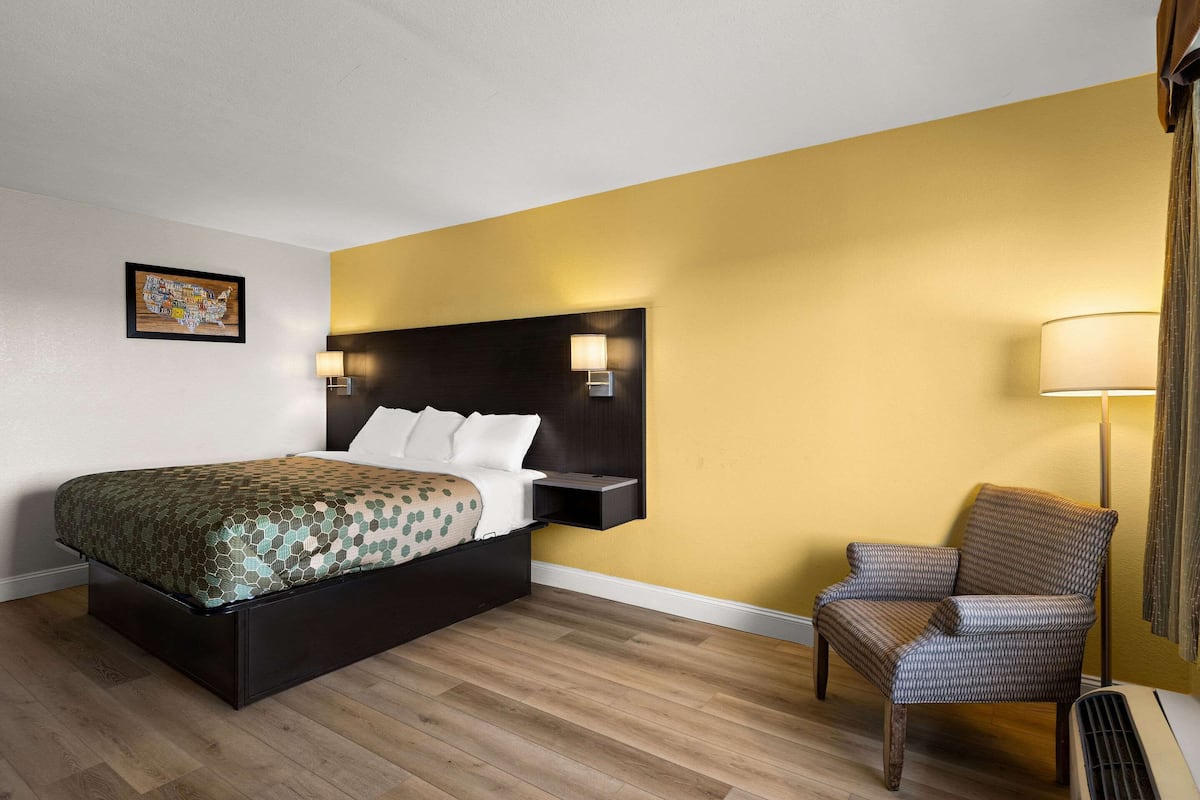 Ein Hotelzimmer mit Bett, Sessel, Wandlampe und einem gerahmten Bild.