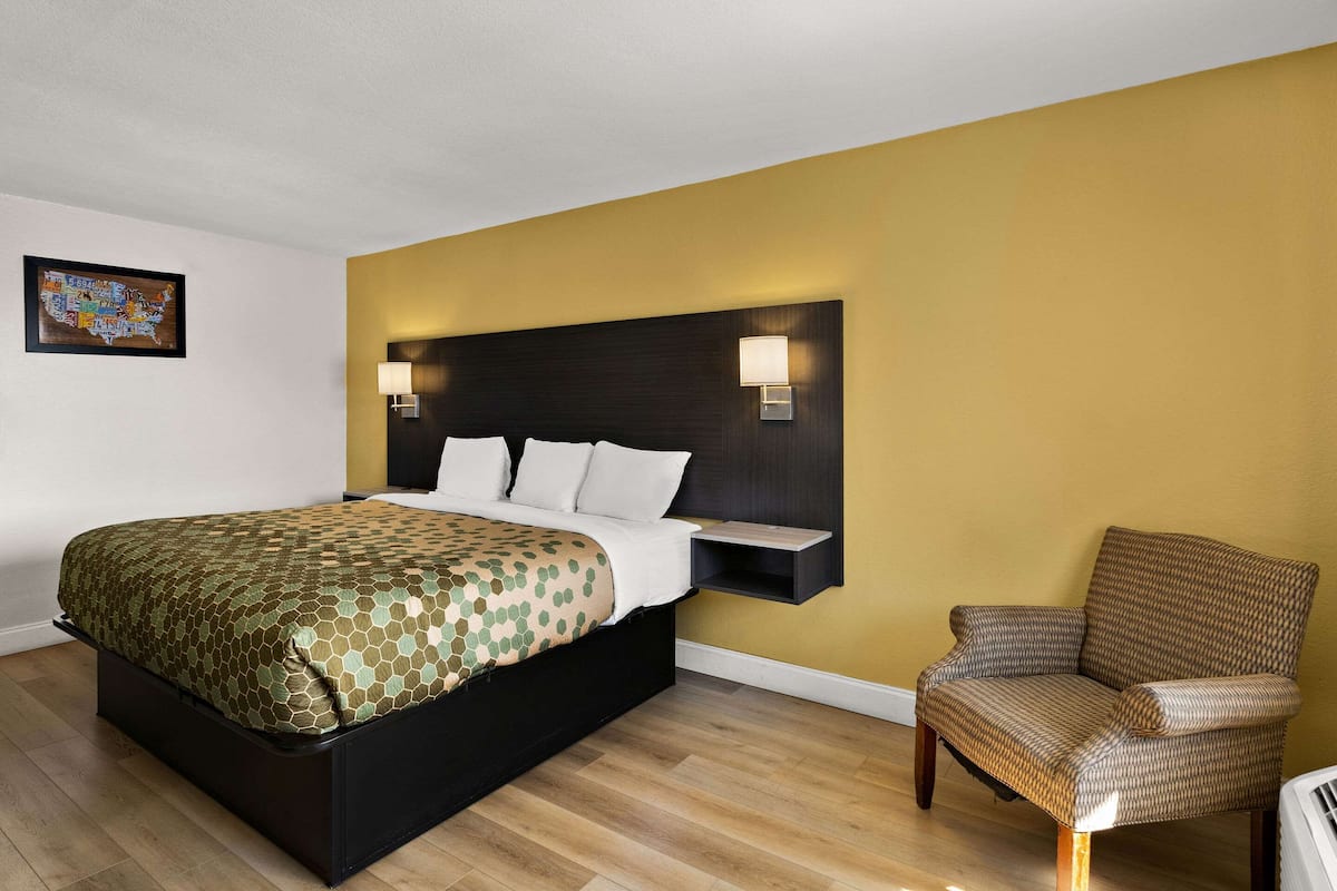 Ein Hotelzimmer mit Bett, Stuhl, Kopfteil mit Wandleuchten und einer Karte an der Wand.