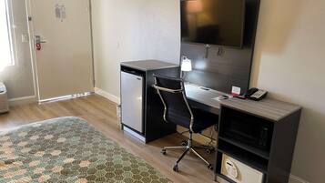 Habitación de hotel compacta con cama, escritorio con computadora, televisión y refrigerador pequeño.