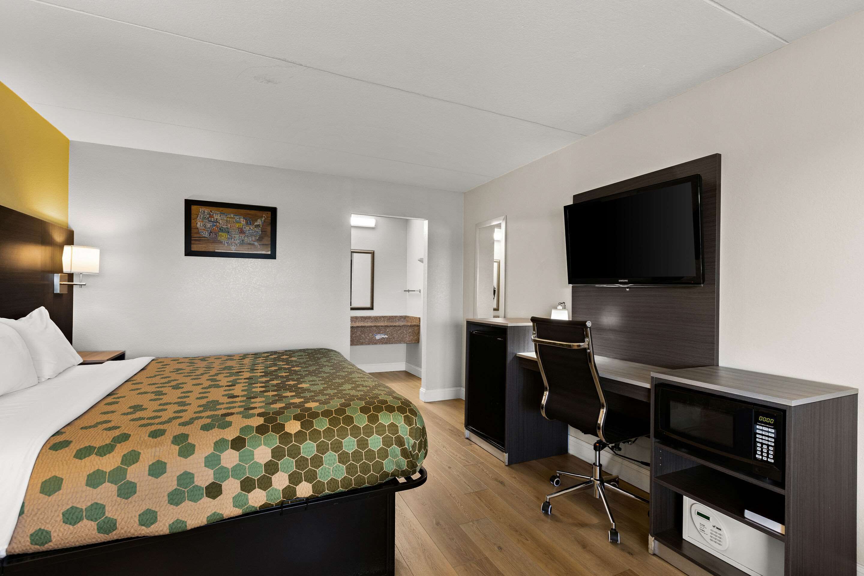 A hotel room with a bed, desk, chair, TV, and microwave.