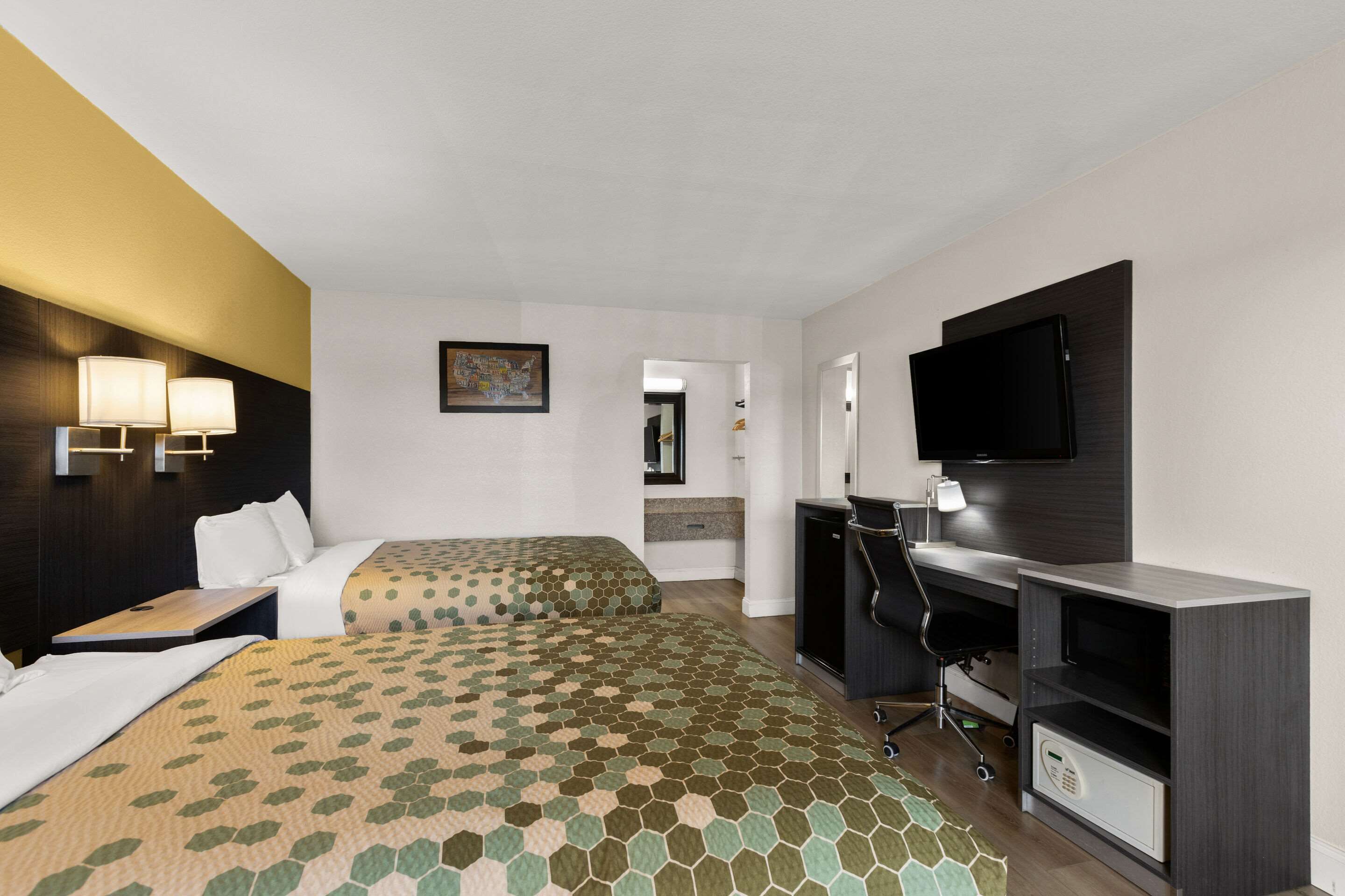 Ein Hotelzimmer mit zwei Betten, einem Schreibtisch, einem Sessel, einem Fernseher und einer Minibar.