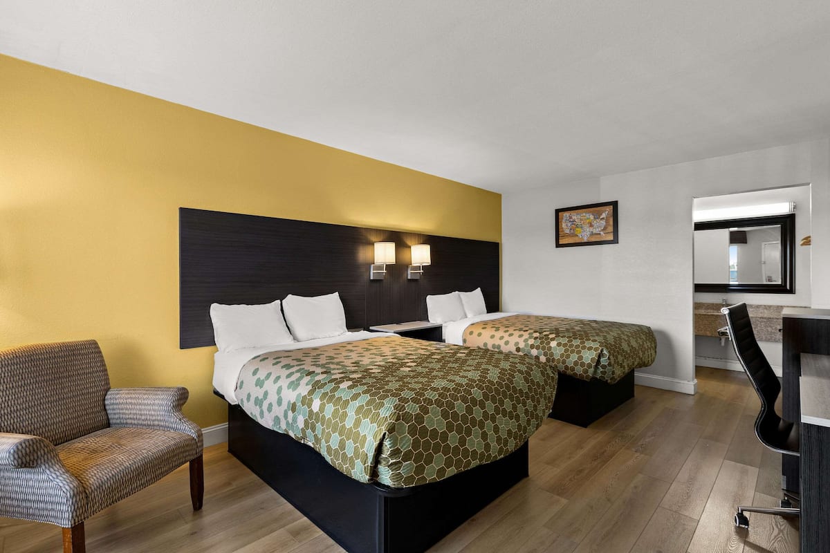 Ein Hotelzimmer mit zwei Betten, einer Schlafcouch, einem Schreibtisch und einem Spiegel.