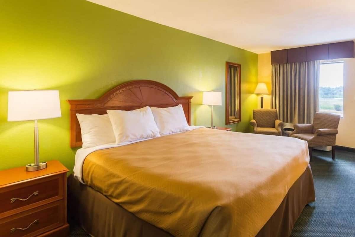 Ein Hotelzimmer mit einem Bett, zwei Nachttischlampen, einem Sessel, einem Schminktisch und einem Fenster mit Vorhängen.