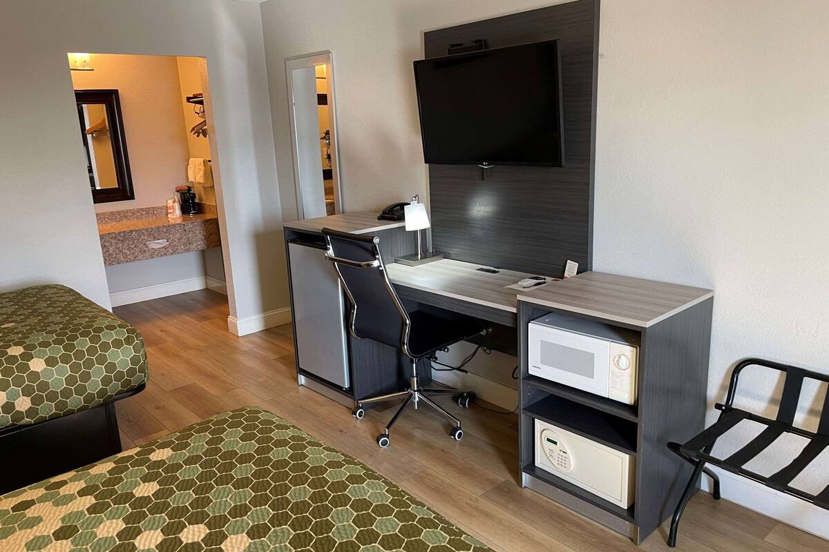 Ein Hotelzimmer mit Bett, Schreibtisch, Computer, Fernseher und Mikrowelle.