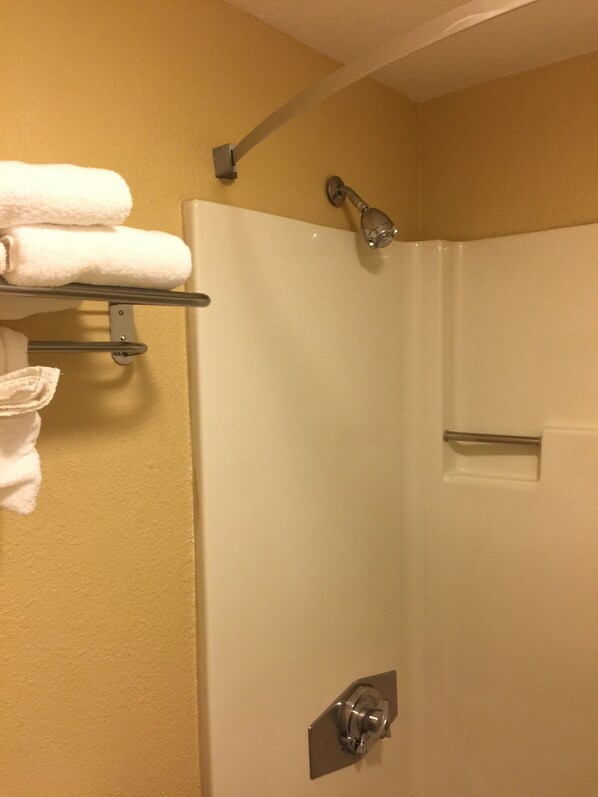 A bathroom with a shower, a towel rack with folded towels, and a shower control panel.