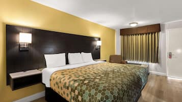 A hotel room with a bed, bedside tables, a chair, a window with curtains, and a door.