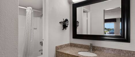 A bathroom with a white bathtub, a sink with a granite countertop, and a large mirror with a black frame.