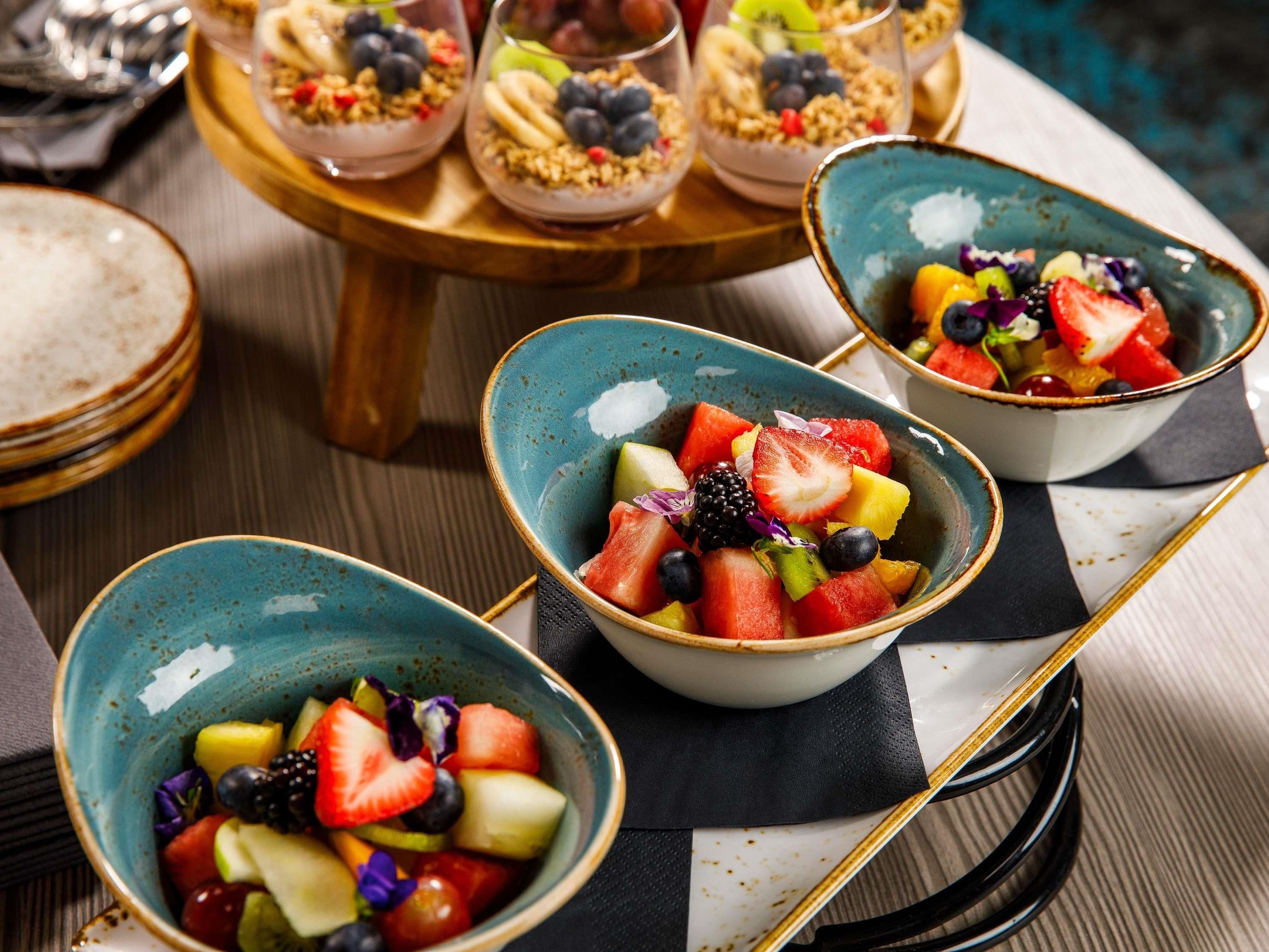 A table with bowls of fruit salad and a stack of pancakes.