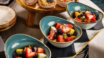 A table with bowls of fruit salad and a stack of pancakes.