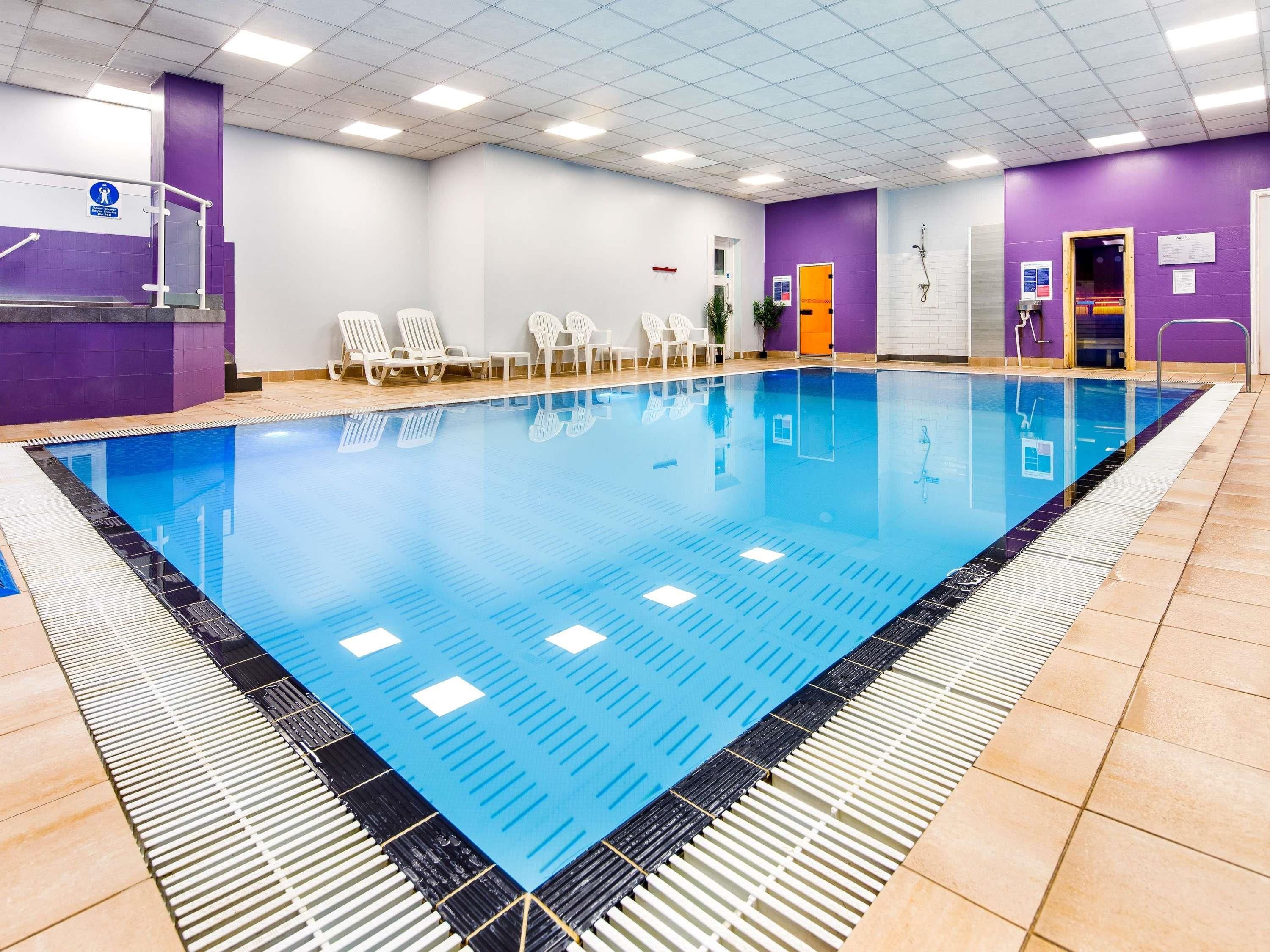 A swimming pool with a tiled deck, lounge chairs, and a changing room with a purple wall.