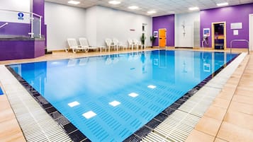 A swimming pool with a tiled deck, lounge chairs, and a changing room with a purple wall.