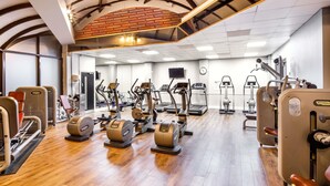 Ein Fitnessraum mit verschiedenen Trainingsgeräten, Holzboden und einer Ziegelwand.