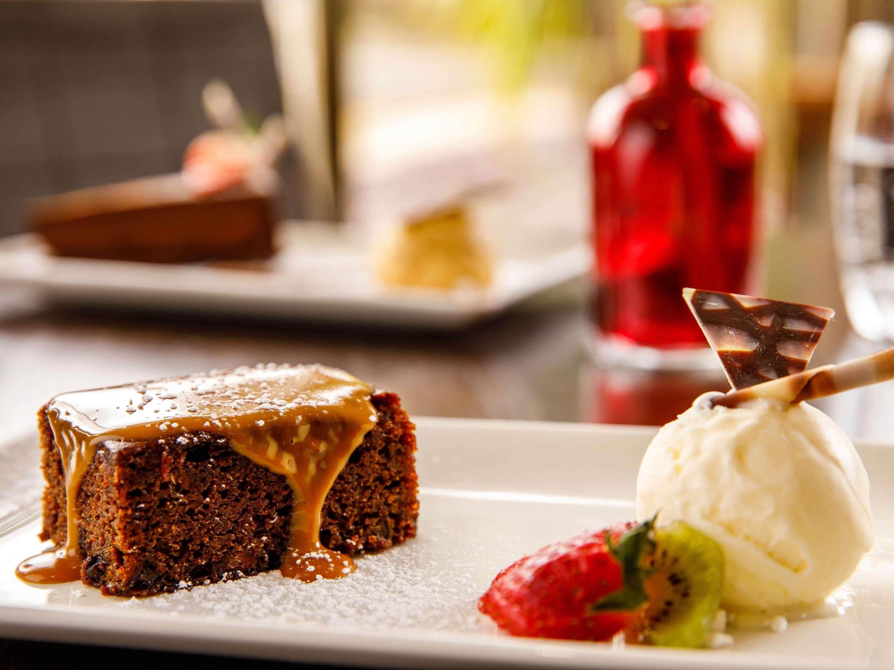 A dessert plate with a slice of cake and a scoop of ice cream, accompanied by a strawberry and a chocolate piece.