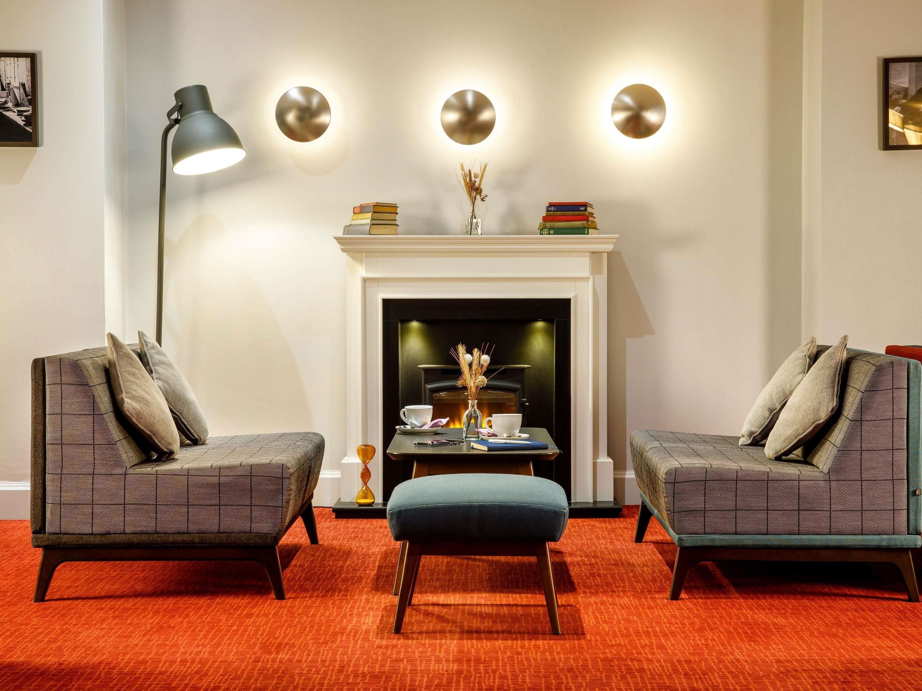 A room with two armchairs, a small table, a floor lamp, a fireplace, and wall-mounted lights.