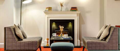 A room with two armchairs, a small table, a floor lamp, a fireplace, and wall-mounted lights.