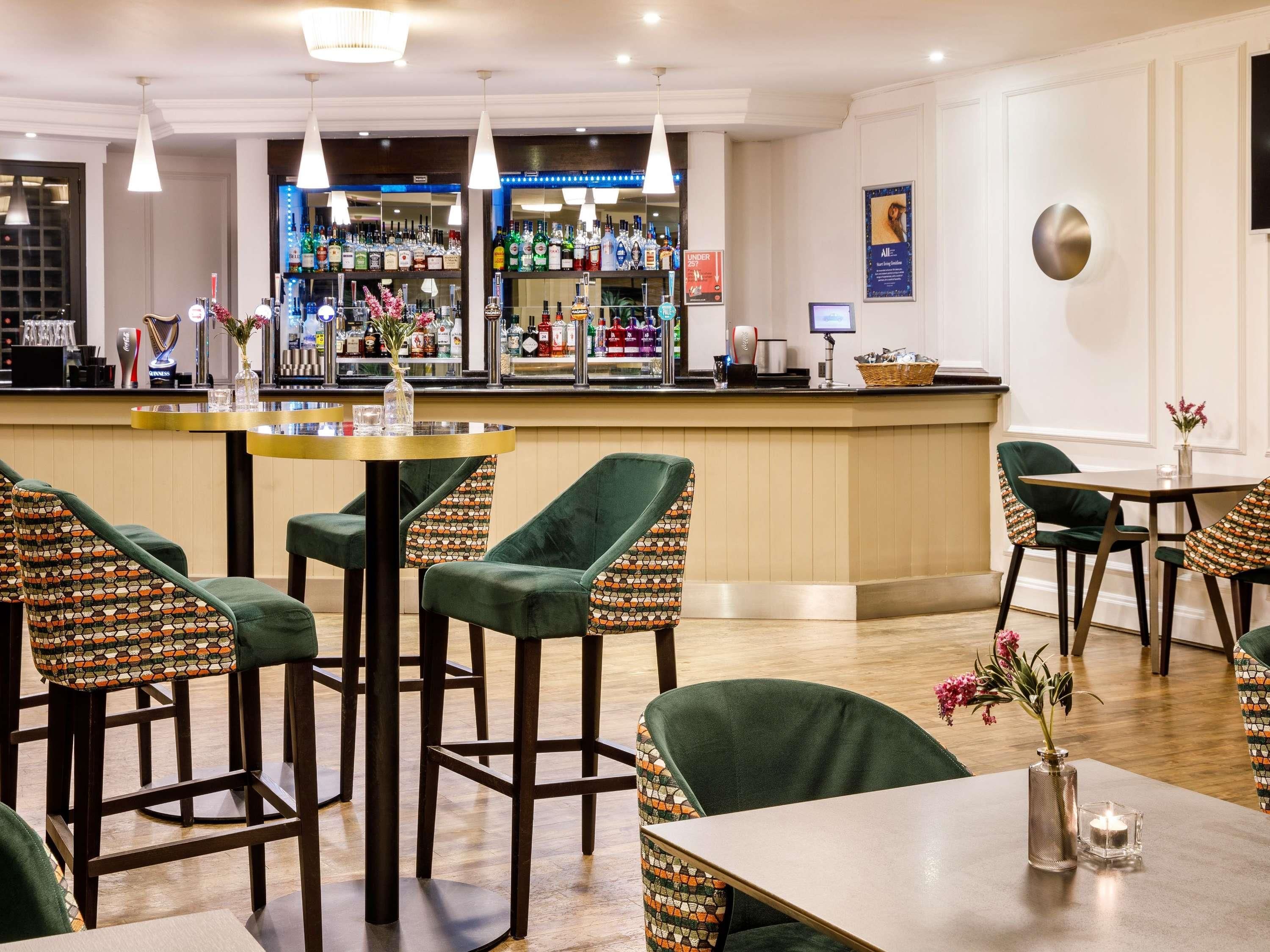 A bar area with stools and tables, a counter with various bottles, and a framed picture on the wall.