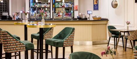 A bar area with stools and tables, a counter with various bottles, and a framed picture on the wall.