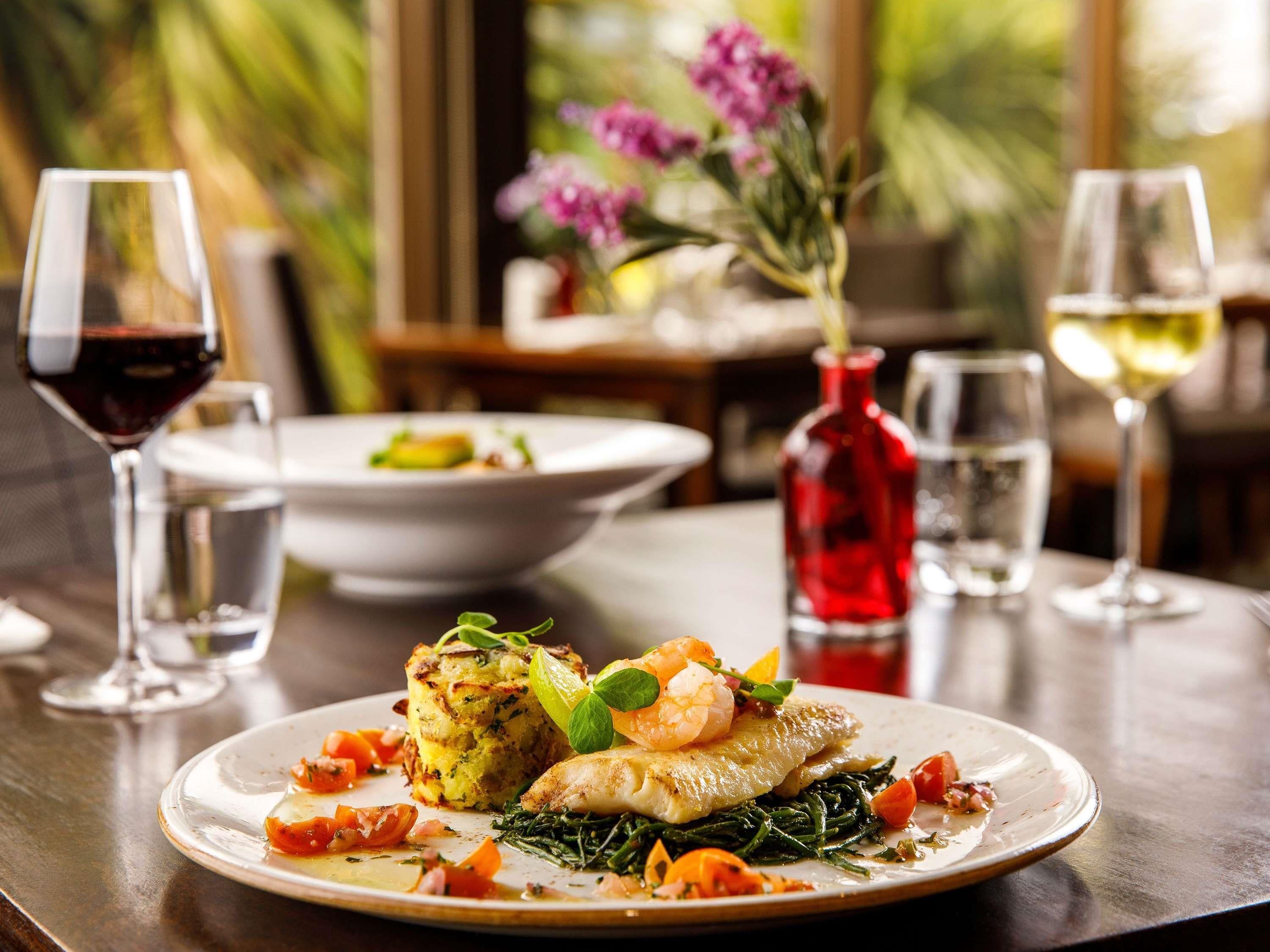 A dining table with a plate of food, glasses of wine, and a red bottle.