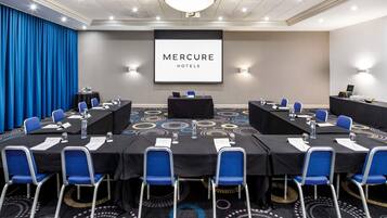A conference room with a large screen displaying 'MERCURE HOTELS,' tables with chairs, and a patterned carpet.