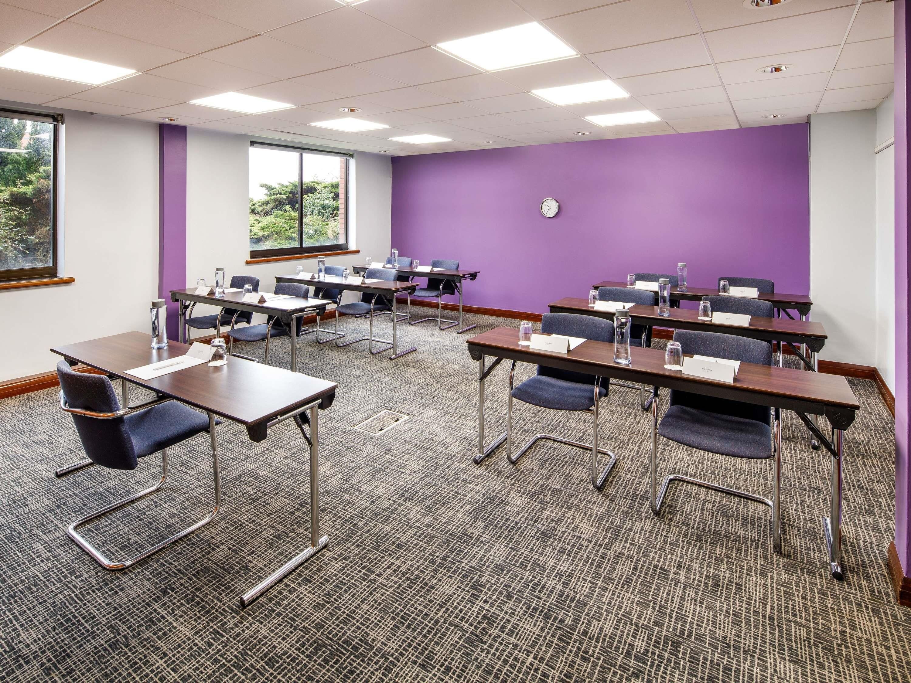 A conference room with multiple tables, chairs, and a clock on the wall.