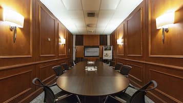 A conference room with a long wooden table, black chairs, and wall-mounted lamps.