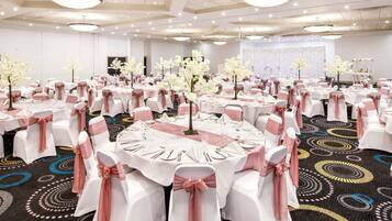 A banquet hall with round tables, white chairs with pink sashes, and floral centerpieces.