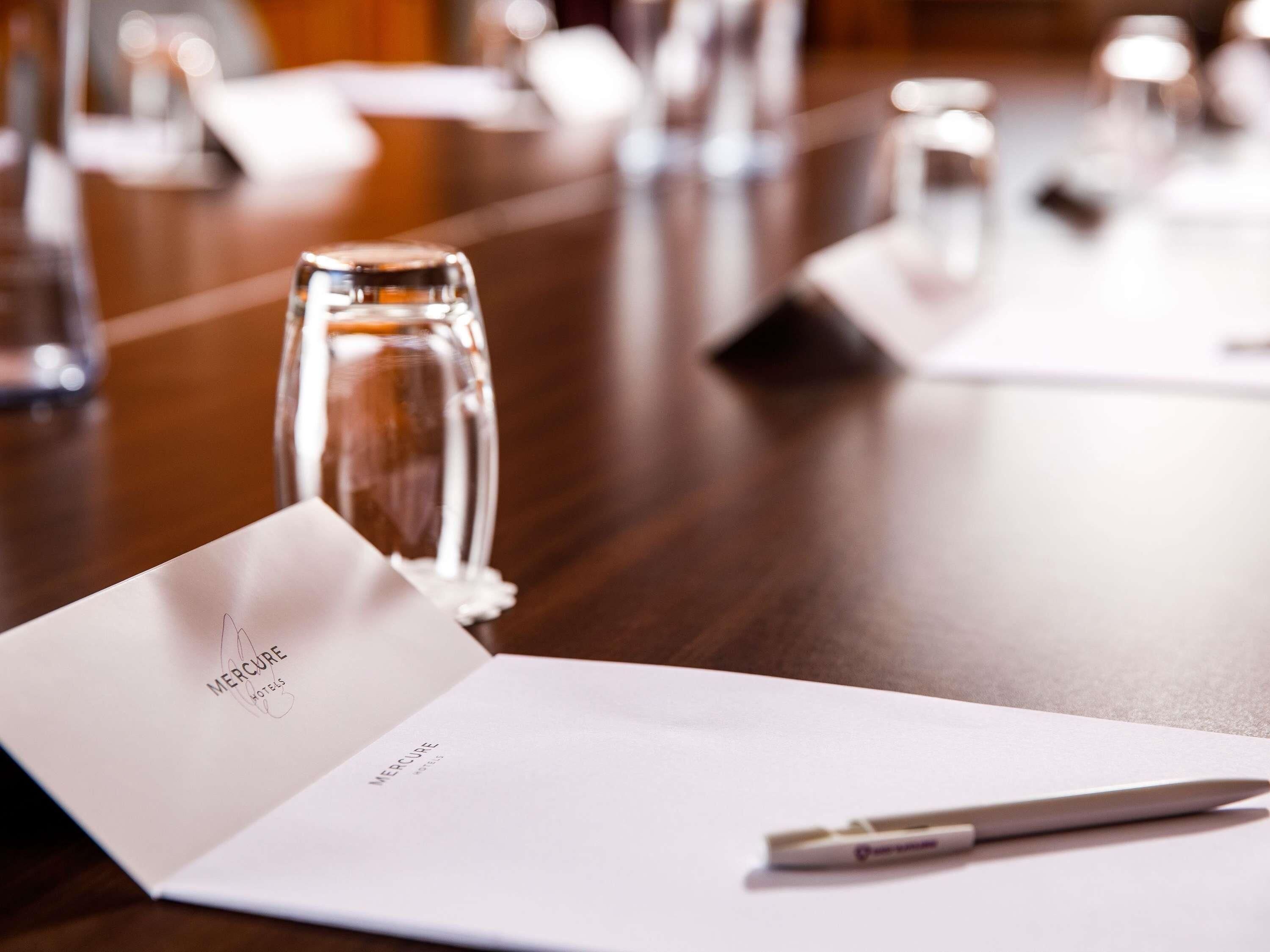 A hotel room with a wooden table, a glass of water, a pen, and a menu.