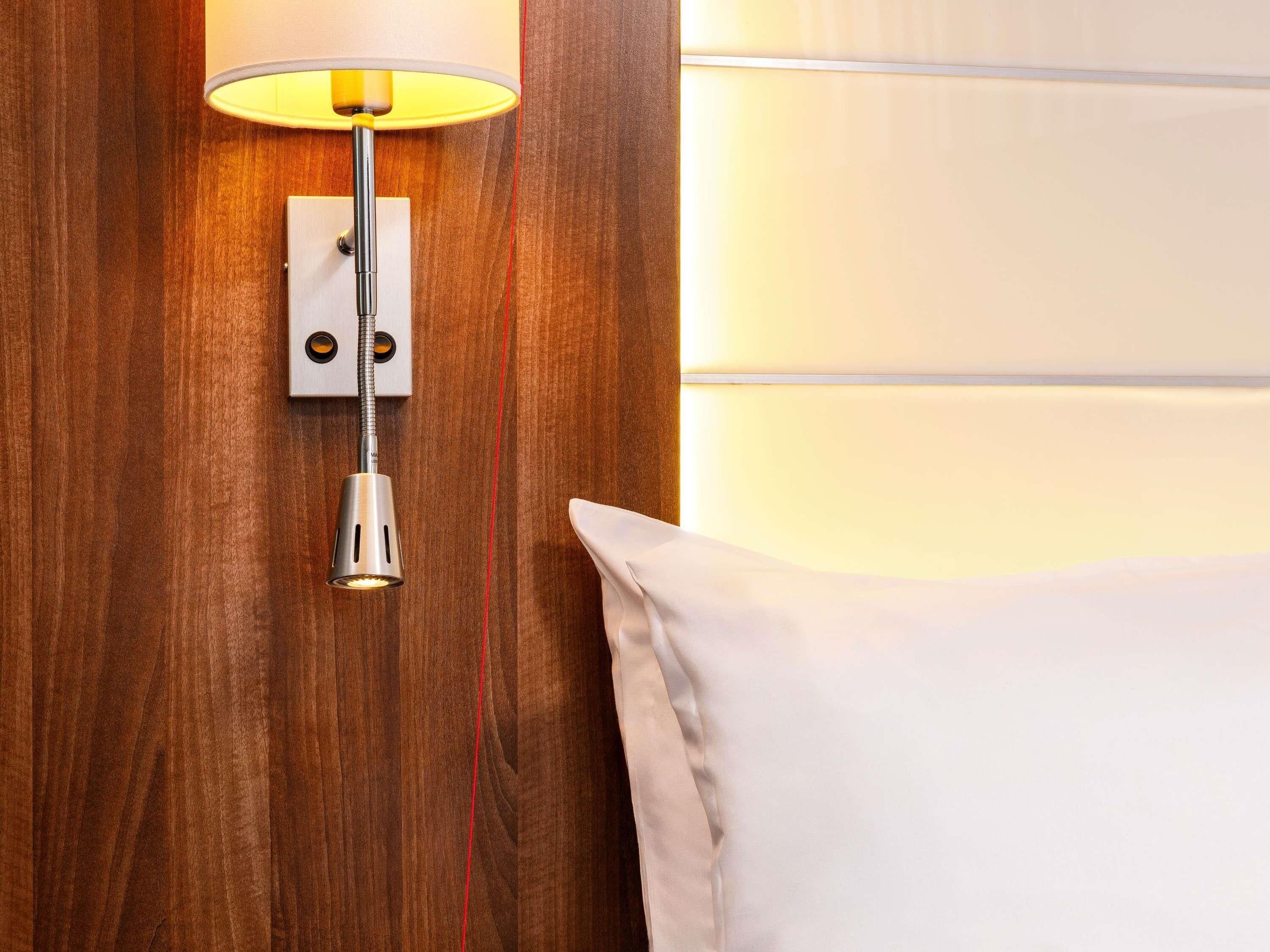Een muurlamp met een witte lampenkap, een stopcontact en een rode kabel.