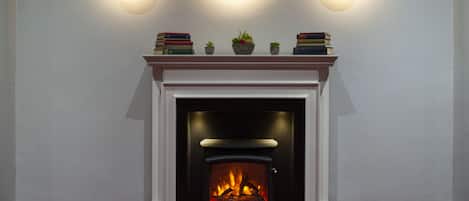 A fireplace with a modern design, a mantel with books and small plants, and three wall-mounted lights.