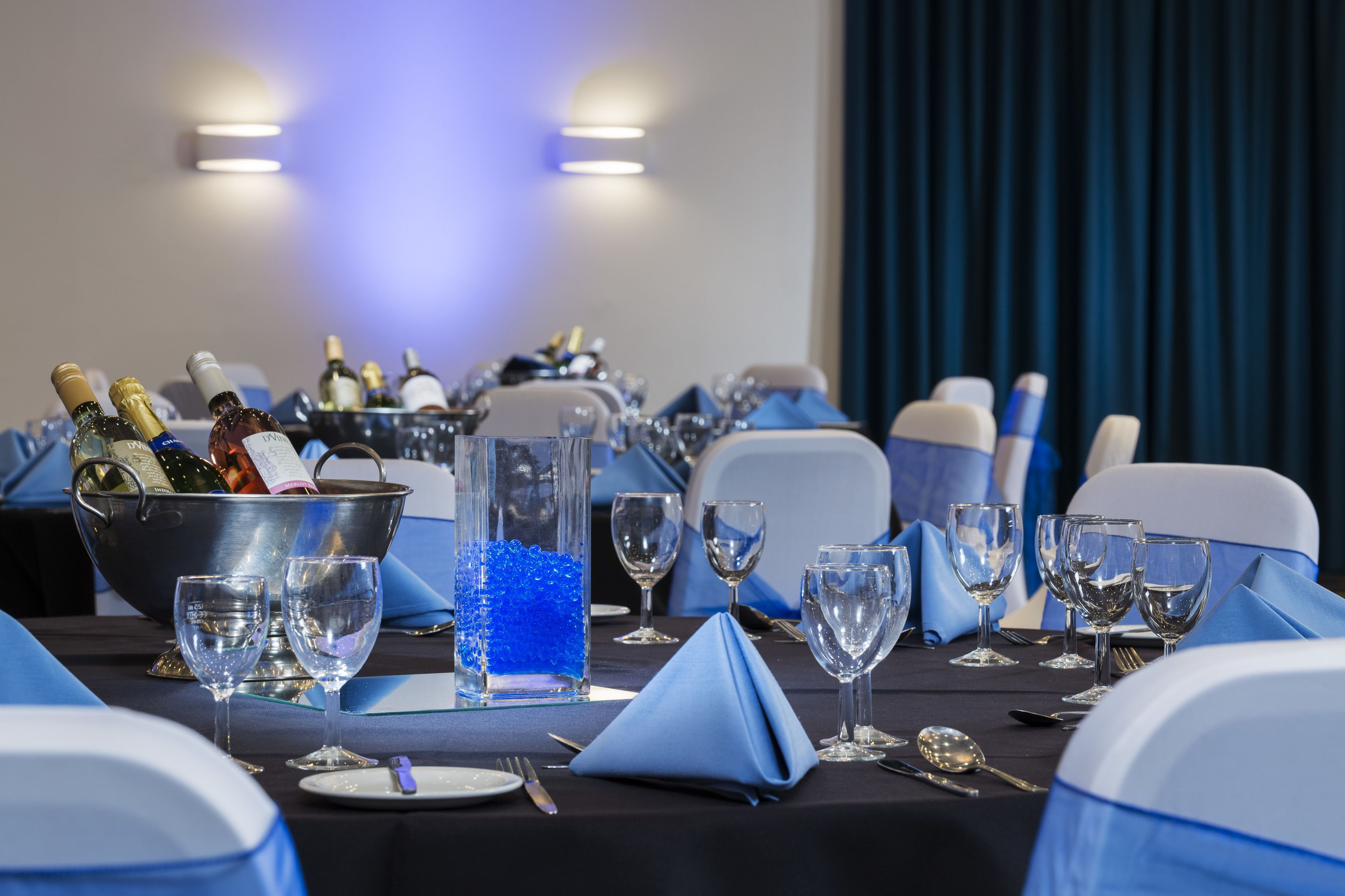 Een feesttafel gedekt met blauwe servetten, wijnglazen en een champagnekoeler.