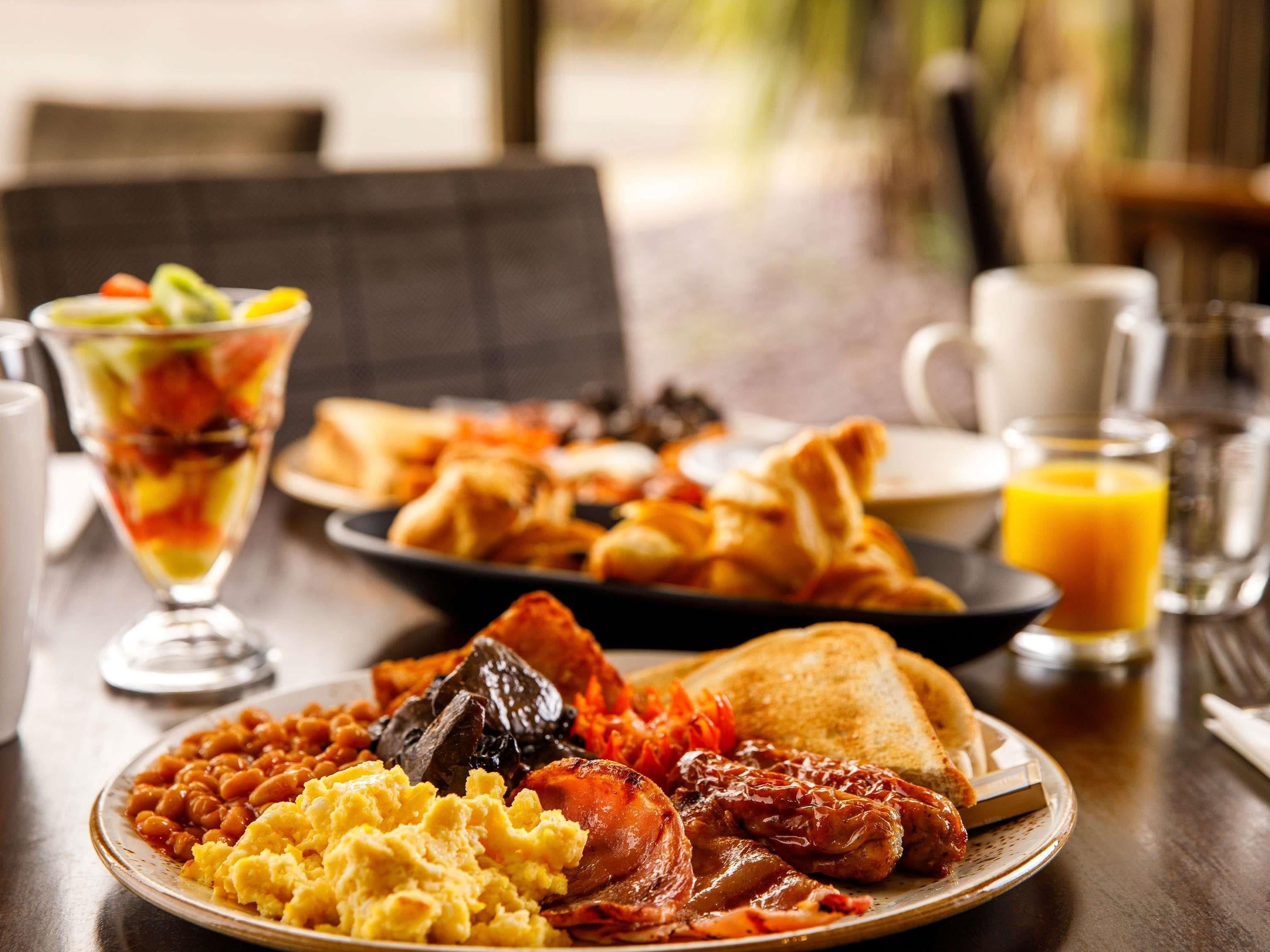 A breakfast plate with beans, scrambled eggs, bacon, toast, and a glass of orange juice.