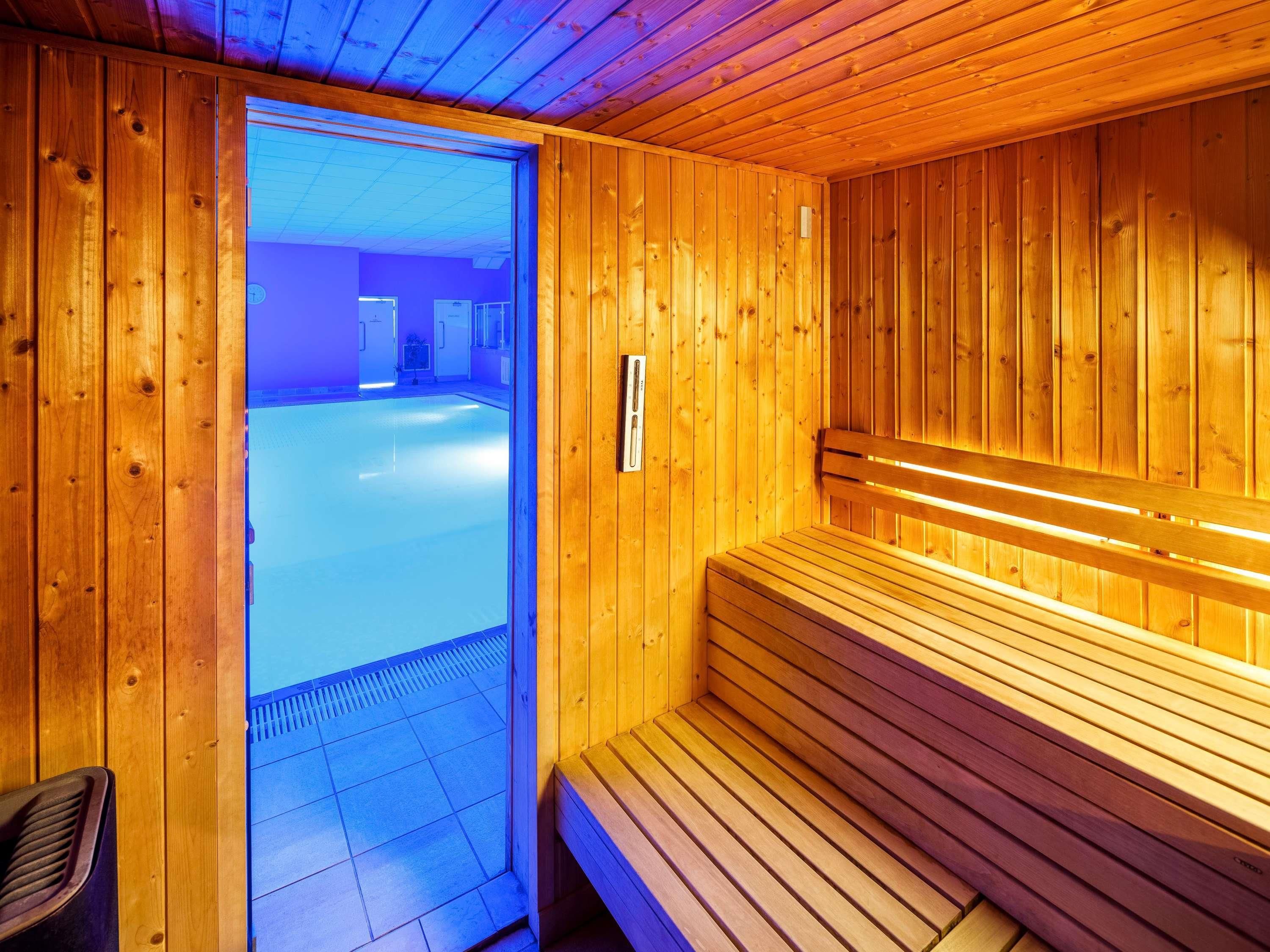Un cuarto de sauna con paredes y bancos de madera, una puerta visible que da al exterior, y un piso de baldosas.