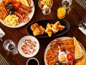 Enjoy a delicious breakfast spread with eggs, sausages, toast, baked beans, croissants, yogurt, and fresh fruit.