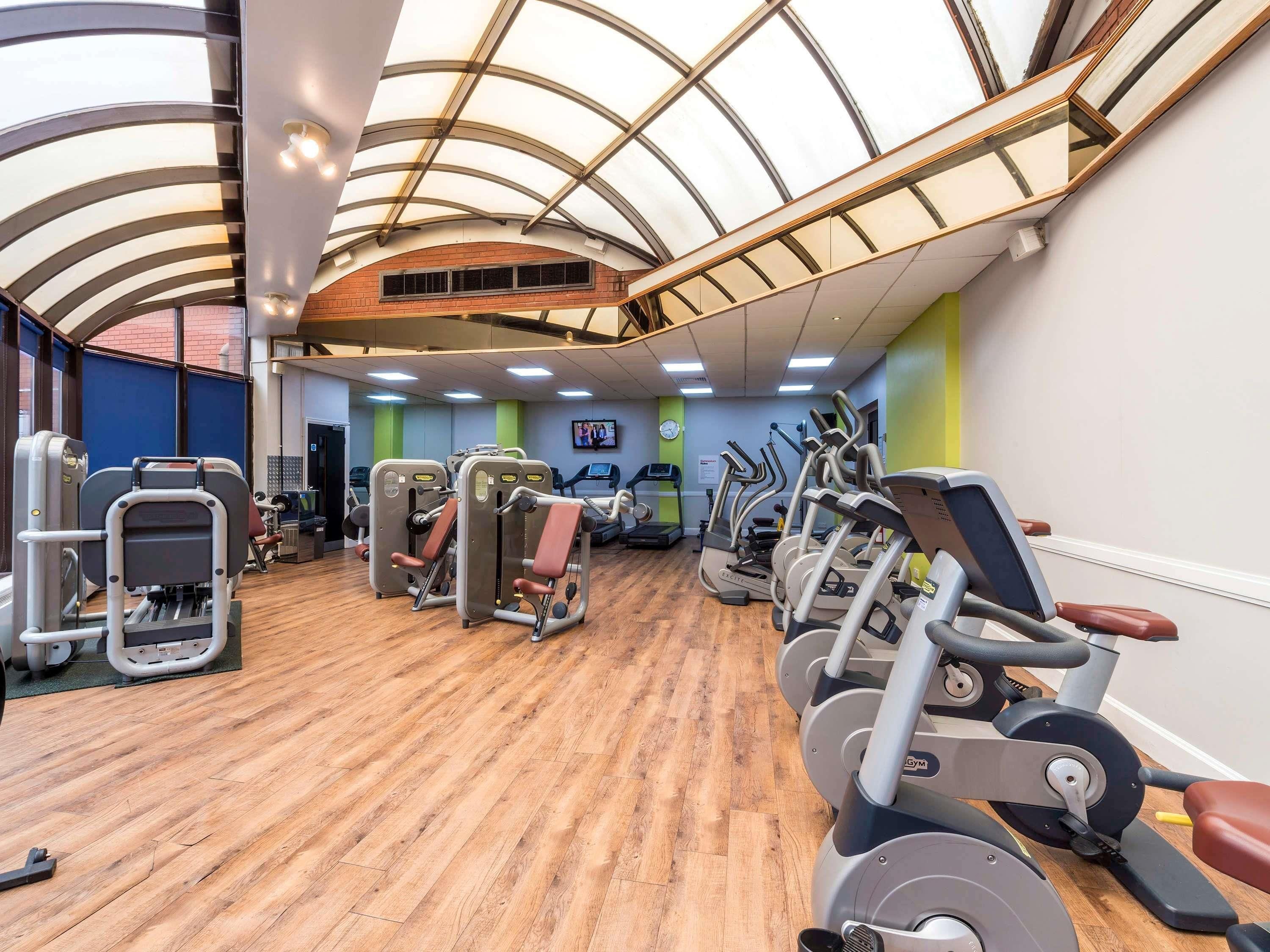 Une salle de sport équipée de matériel d’exercice, dotée d’un plancher en bois et d’un plafond haut avec des fenêtres de toit.