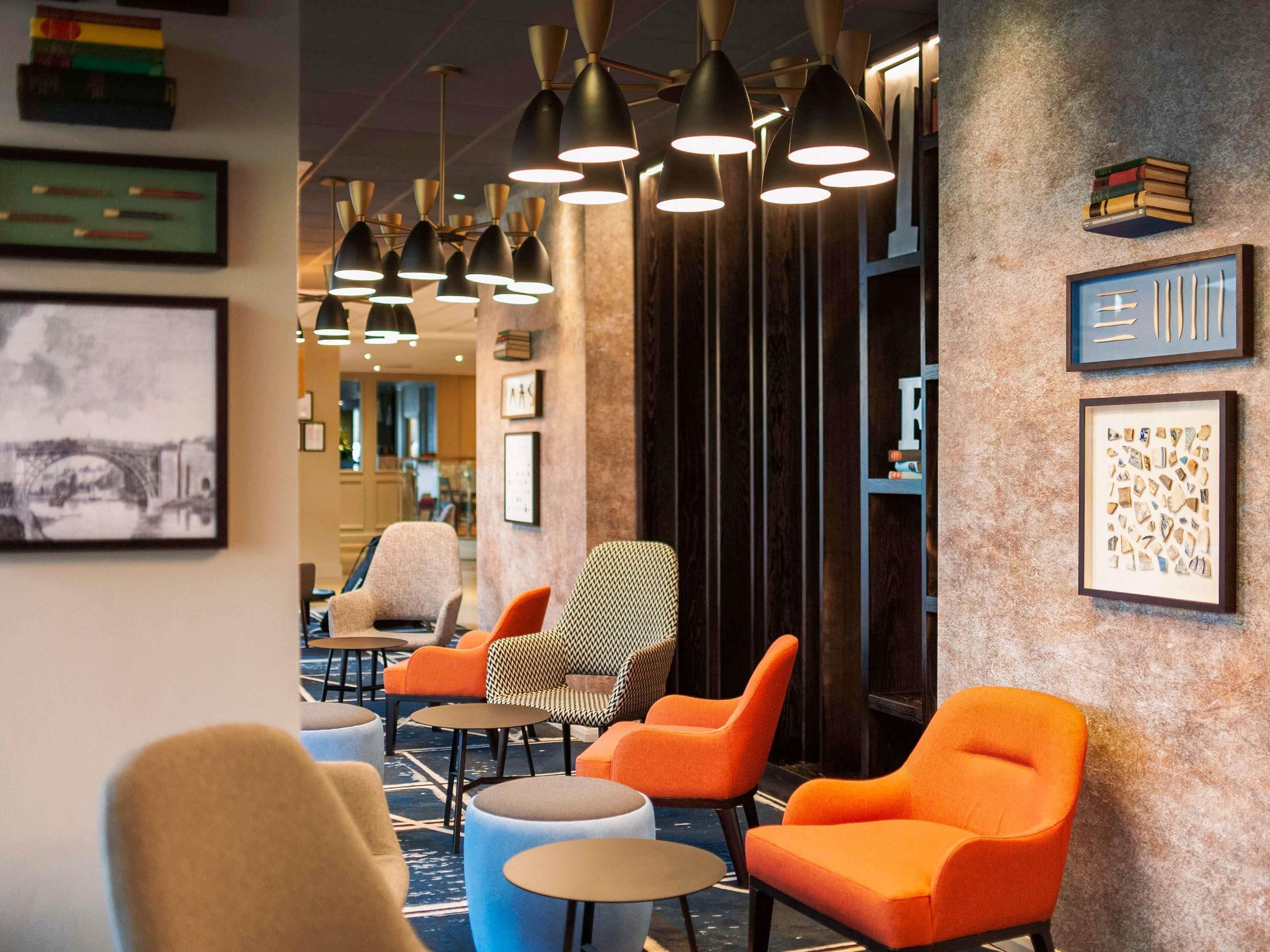 A modern lounge area with multiple seating options, including orange and beige chairs, and a variety of pendant lights.
