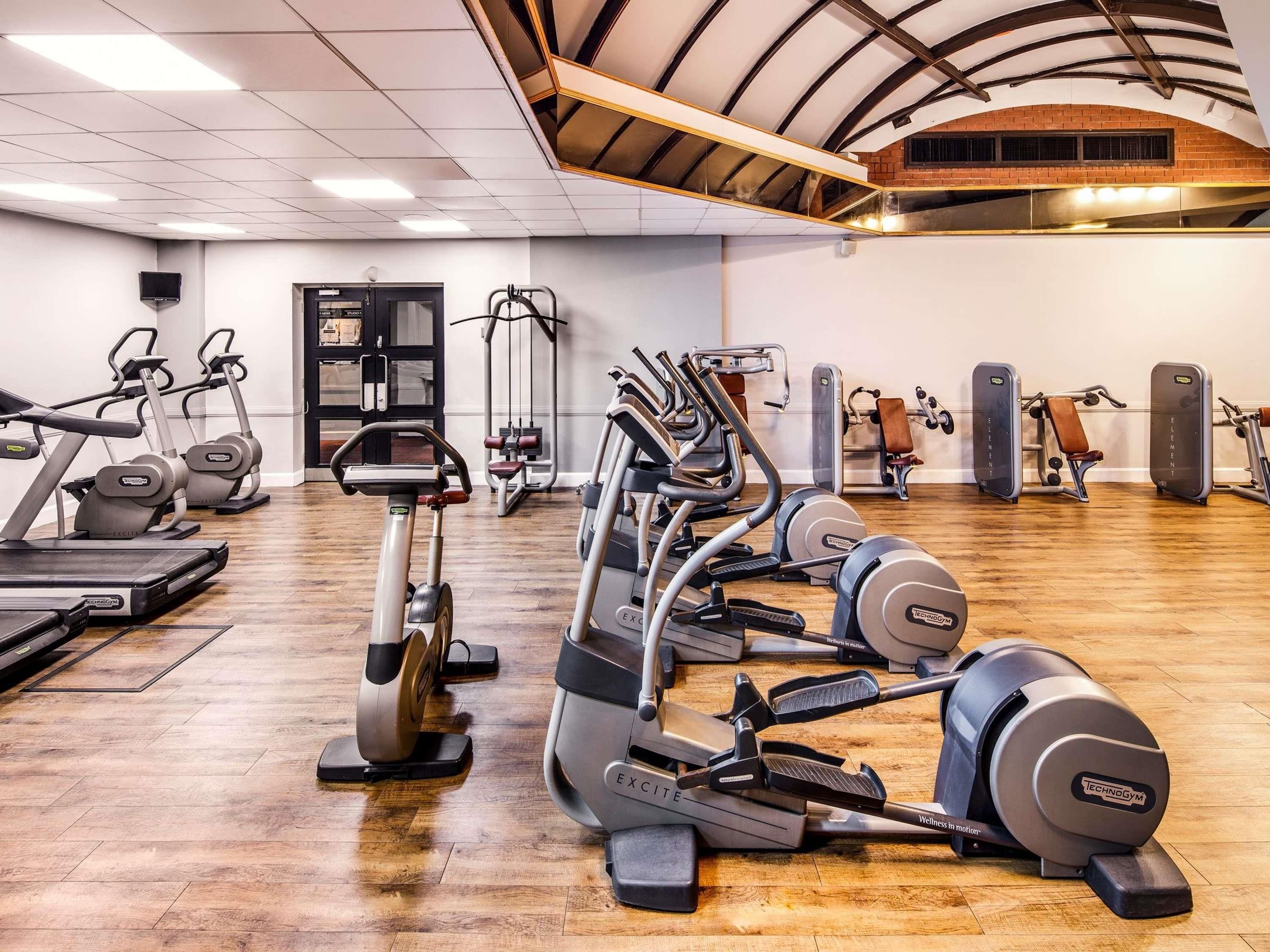 Un gimnasio con diversos equipos de ejercicio, incluyendo cintas de correr, elípticas y máquinas de pesas.