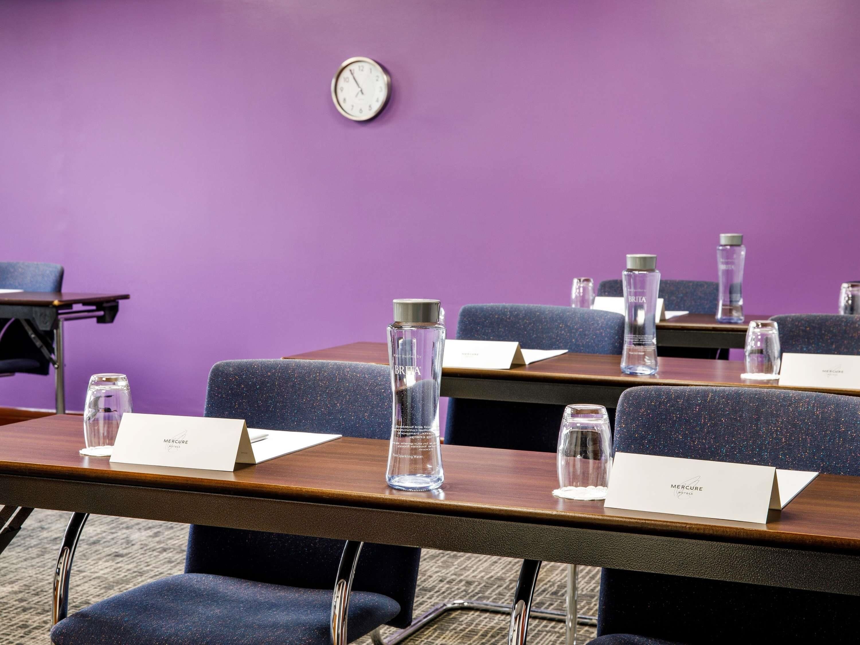 A conference room with tables, chairs, name cards, water bottles, and a clock on the wall.