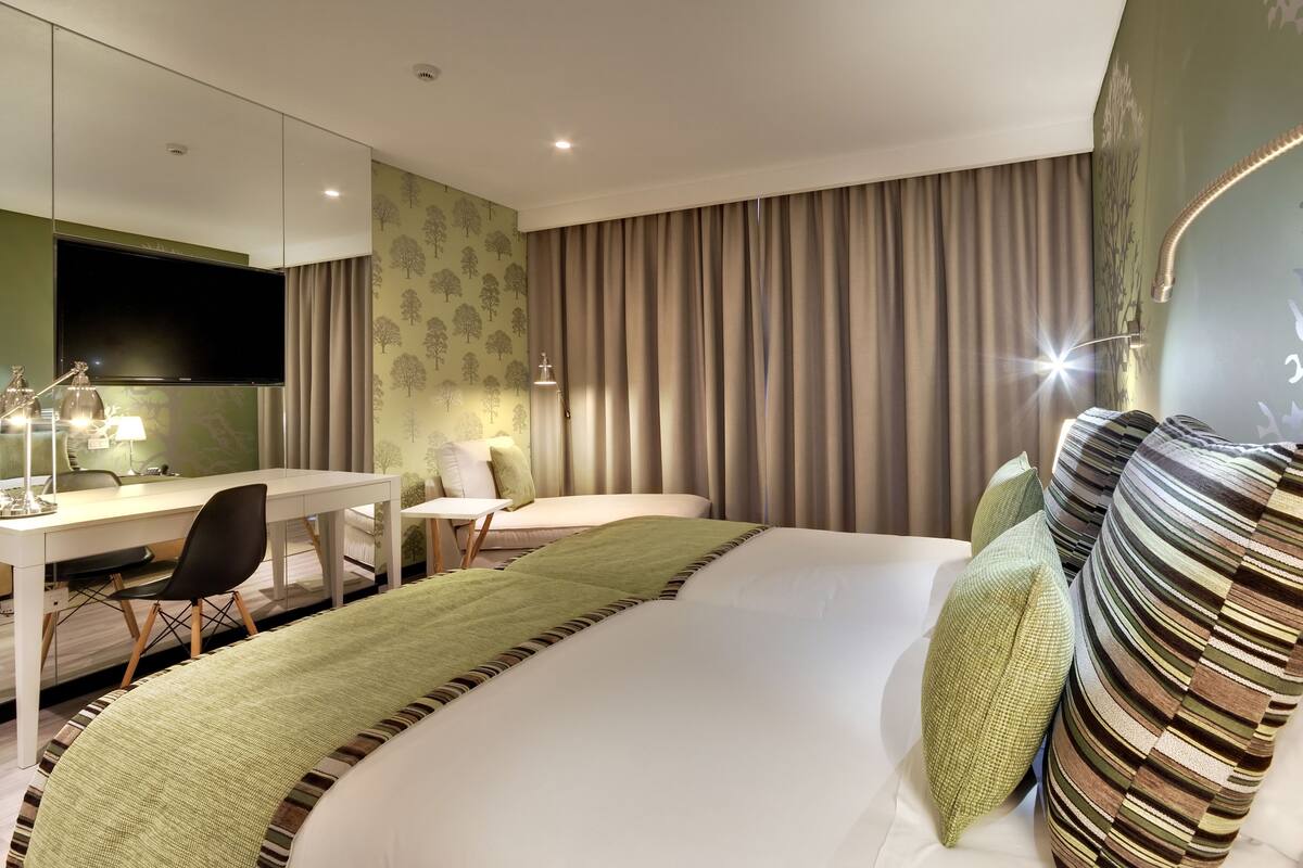 A hotel room with a bed, a desk, a chair, a TV, and curtains.