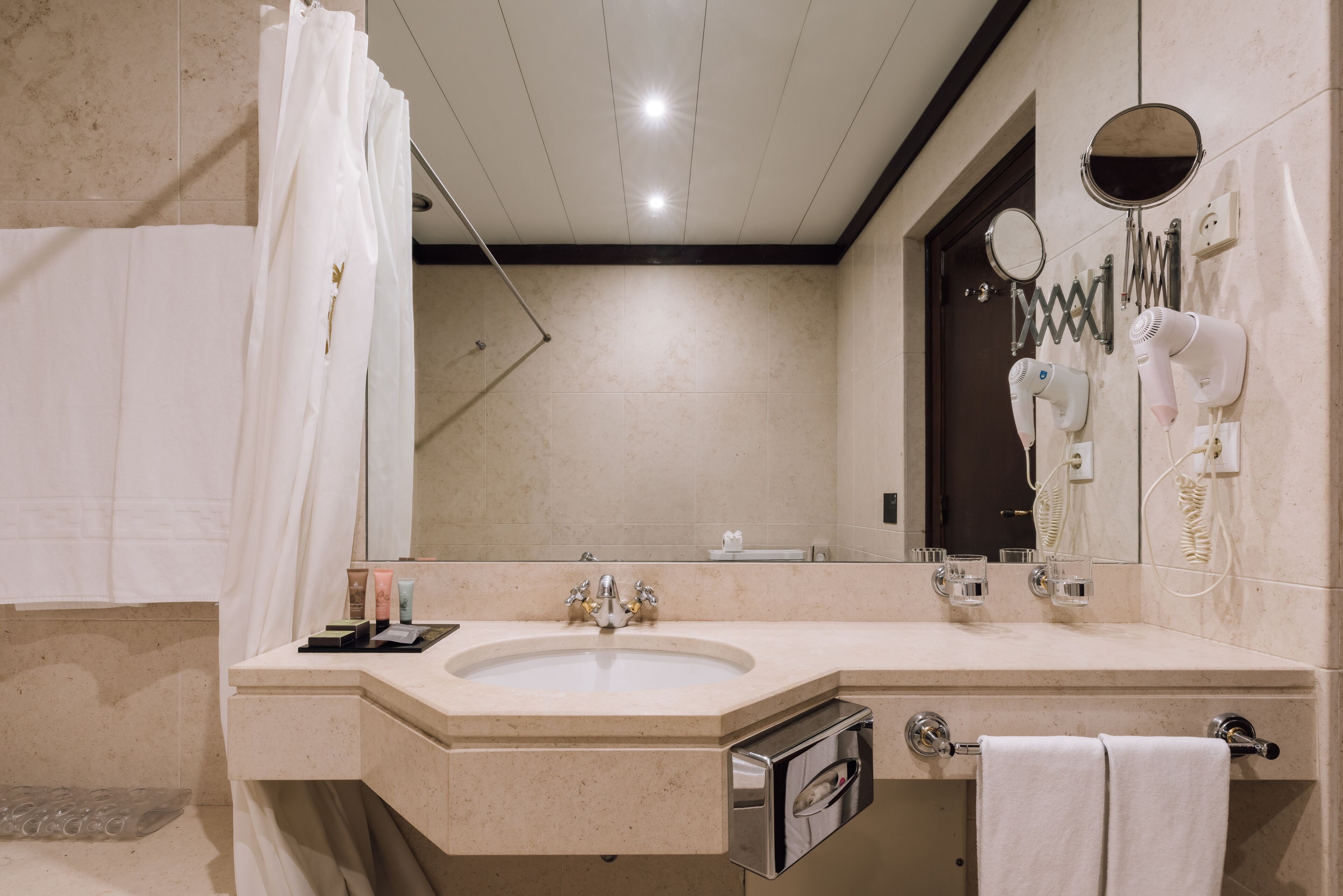 Une salle de bain moderne équipée d’un lavabo, d’un miroir, d’un porte-serviettes et d’un sèche-cheveux.