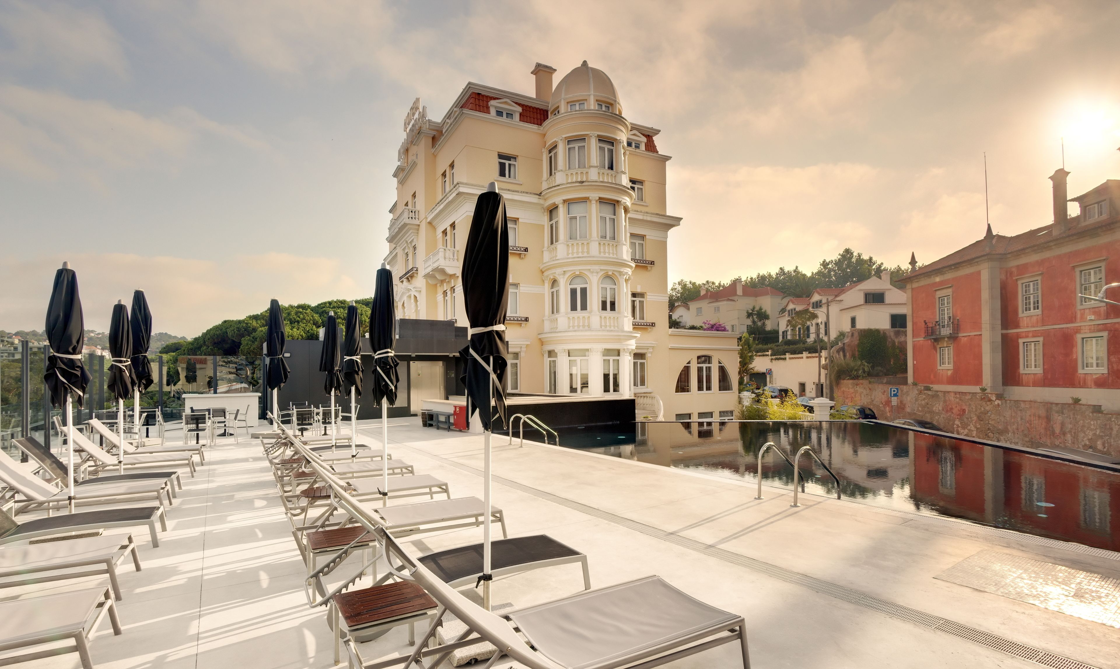 Una terraza en la azotea con tumbonas y sombrillas, piscina y vistas a edificios históricos.