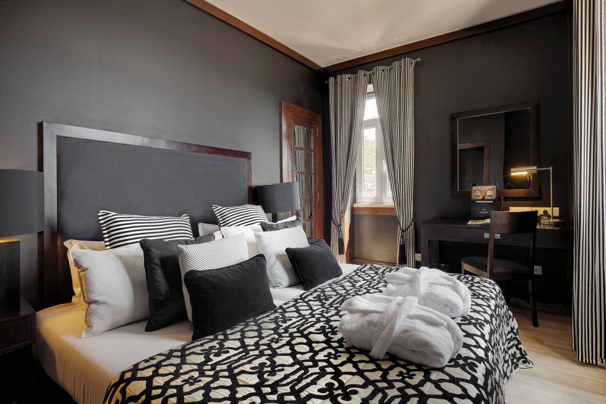 A hotel room with a bed, bedside table, and a desk with a chair.