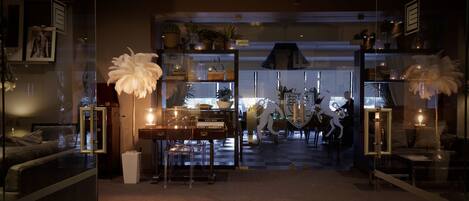 A modern interior with a checkered floor, a central table with a candle, and decorative items including a white feather sculpture and a glass cabinet.
