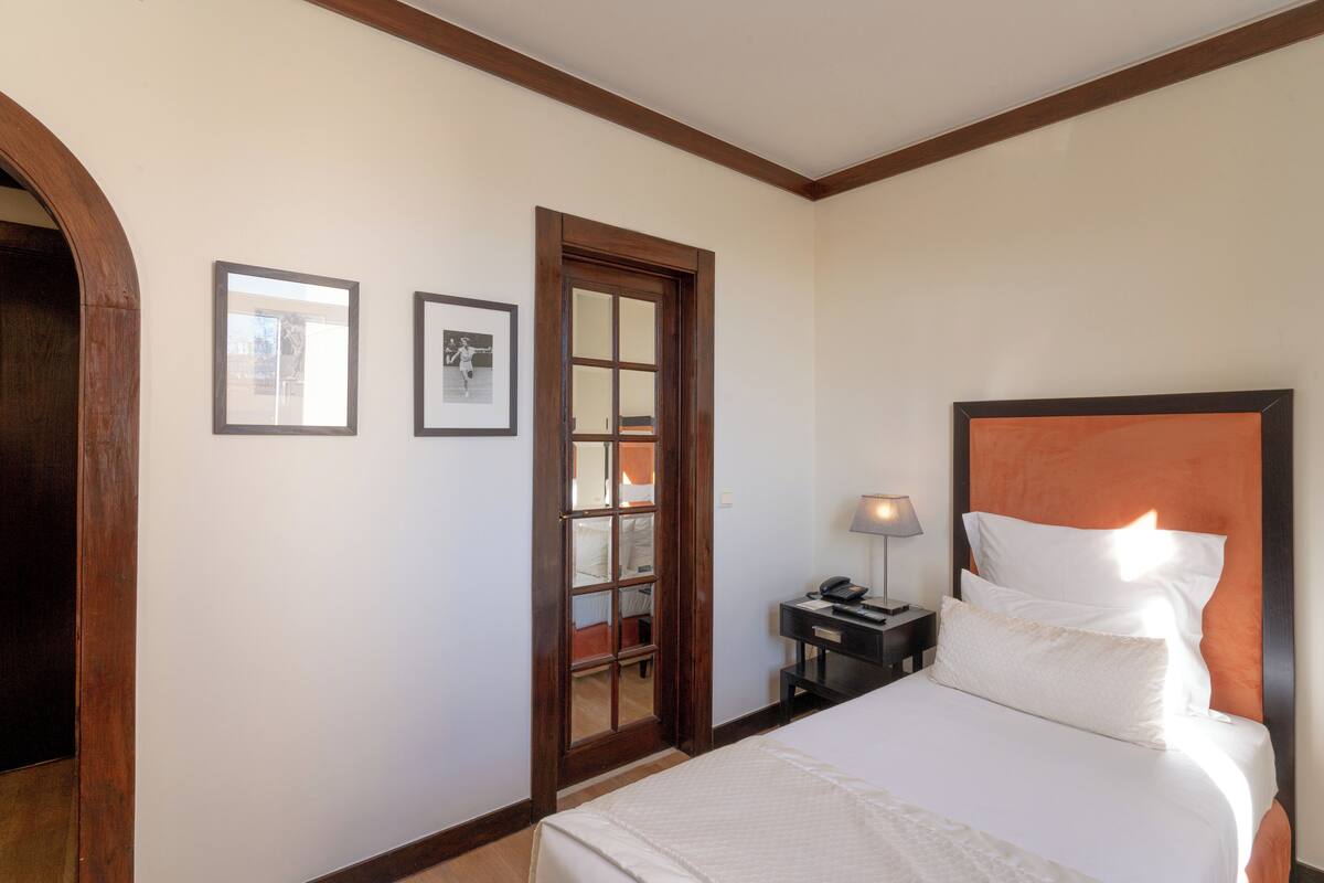 A hotel room with a large bed, a wooden door, and a small bedside table with a lamp.